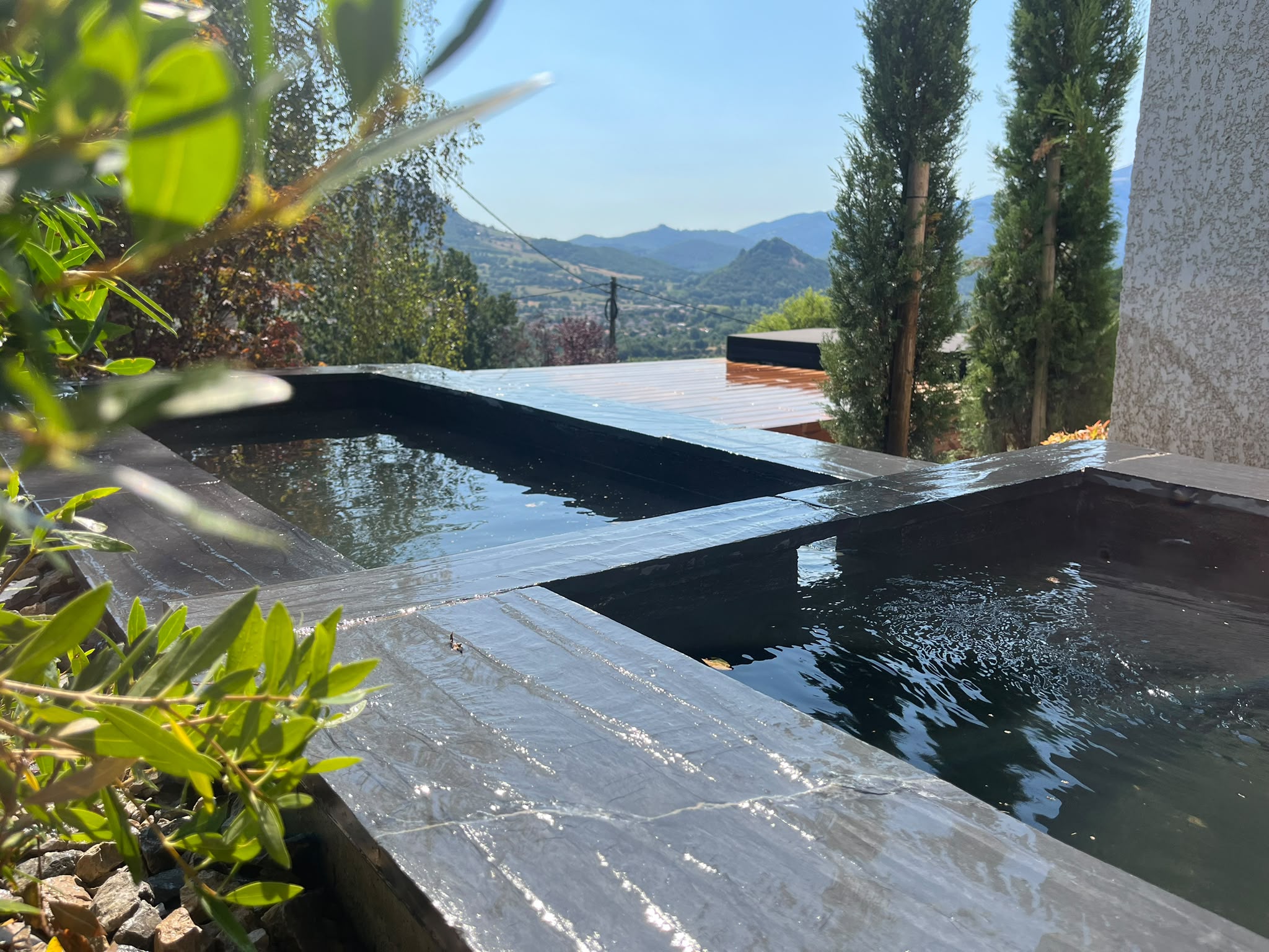 Bassin contemporain en pierre noire par jardins-paysages dans un jardin avec vue sur les montagnes en Ariège
