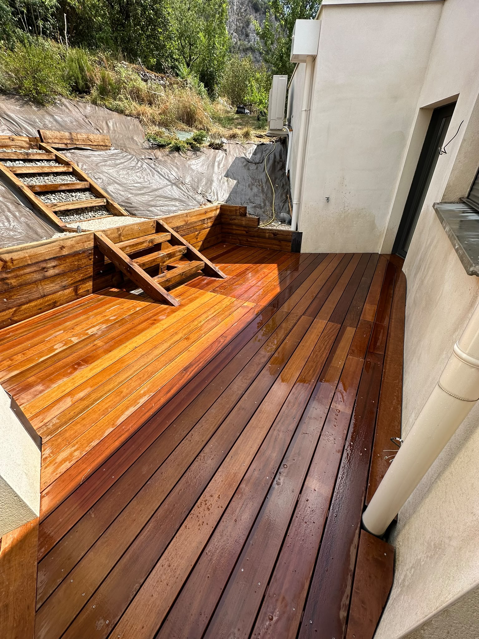 Terrasse en bois brillante avec mur de soutènement et jardin verdoyant par jardins-paysages en Ariège